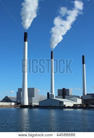 Ciminiere a pianta di energia con cielo blu e lago