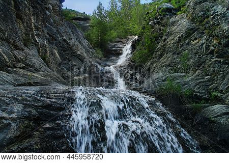 High In The Altai Mountains, A Waterfall Flows Along A Depression In The Rocks, Trees Grow Above, Su