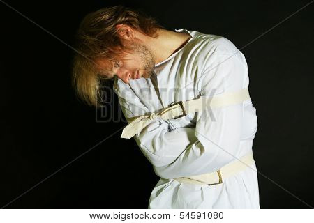 Mentally ill man in strait-jacket on black background