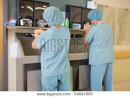 Rear view of female surgeons washing hands at washbasin in hospital