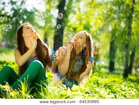Beauty teen girls having fun outdoors. Beautiful joyful teenagers laughing and blowing soap bubbles in spring park. Girlfriends outdoor. 