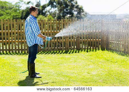 young man watering backyard lawn using hosepipe