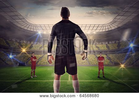 Composite image of goalie facing opposition against large football stadium with lights
