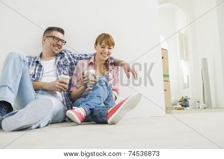 Full-length of cheerful couple with coffee cups in new house
