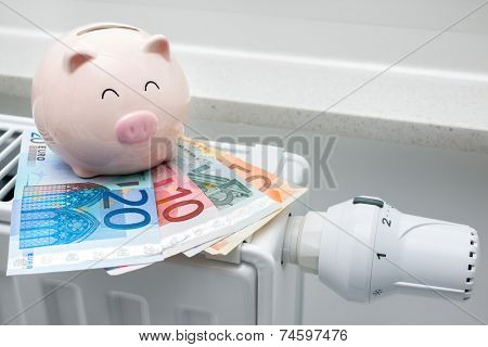 Heating thermostat with piggy bank and money, expensive heating costs concept