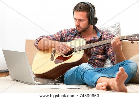 Man on sofa playing the guitar with laptop at home