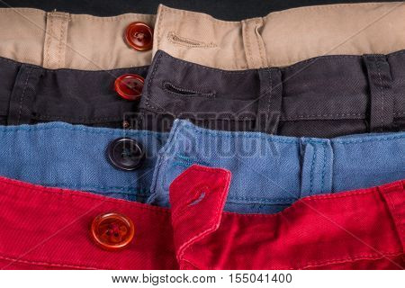 Fragment Of Four Cotton Twill Pants Red, Blue, Black, Beige With Open Buttons. Close Up.
