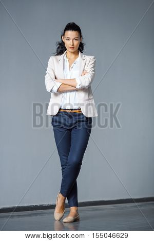 Beautiful brunette business woman in suit posing outdoors against gray background and looking at camera in full lenght. Copy space