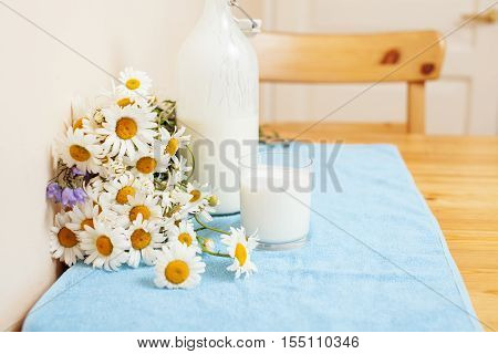 Simply stylish wooden kitchen with bottle of milk and glass on table, summer flowers camomile, healthy foog moring concept noone close up