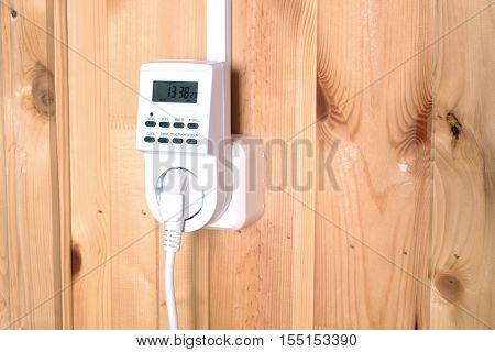 Working white electric timer socket plug operated smart house system against wooden wall inside room side view closeup