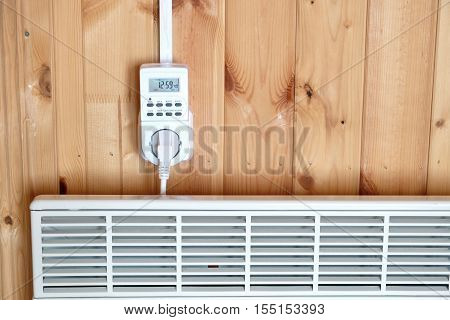 Working white electric convector heater plugged to timer power socket operated in smart house system against wooden wall inside room front view closeup