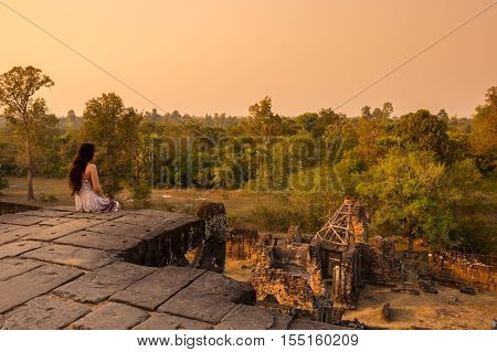 ANGKOR WAT CAMBODIA - JANUARY 28 2015: Young beautiful woman watching sunset at the top of Phnom Bakheng at Angkor Cambodia