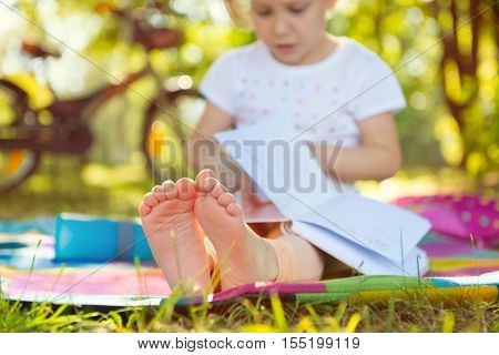 Cute Child Sitting On Grass With Book. Foots In Focus