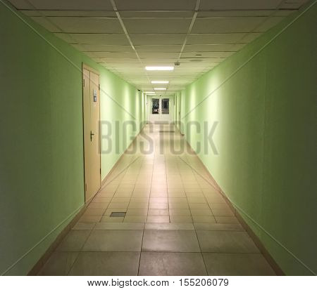 Modern interior in office building. Long empty hall with distant doors and office entrance. Inside an official workspace: hospital, school, company's department. Business look space with green walls