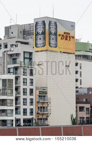 Tokyo Japan - September 28 2016: An Asahi Super Dry lager beer can billboard on top of some older apartment buildings along the Sumida River. Mostly white buildings gray sky. Beer Sign adds the color.