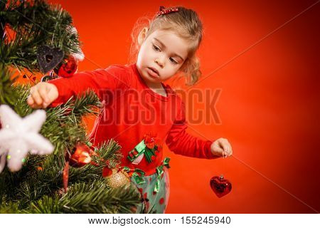 pretty little girl decorates the Christmas tree with beautiful balls