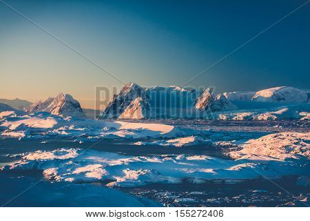 Antarctic landscape with snow covered mountains against blue sky. Sunset warm light on the mountain peak. Exploring beauty world