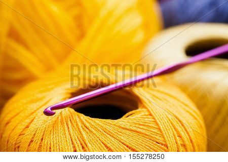Yellow thread with crochet close-up, handiwork background. Several balls of xanthous yarn with knitting tool. Leisure, hobby, bright needlework backdrop