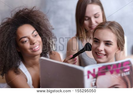 Enjoyable process. Pleasant smiling involved girls reading the magazine and sitting on the bed while getting ready for a party