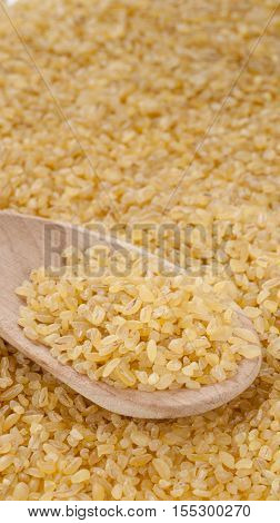 bulgur in wooden spoon close up. Vertical with copy space