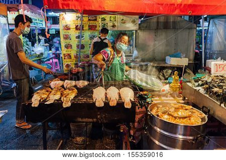 CHIANG MAI THAILAND - AUGUST 27: Thai woman cooks grilled fish at the Saturday Night Market on August 27 2016 in Chiang Mai Thailand.
