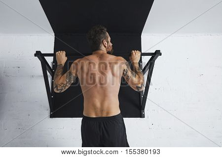 Back view on muscular topless male athlete showing calisthenic moves Pull up on pullbar, head looking on rightside direction