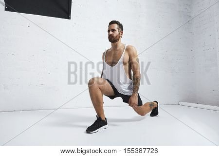 Strong tattooed in white unlabeled tank t-shirt male athlete shows calisthenic moves Lunges, looking on side