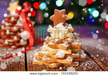 Home made baked Christmas gingerbread tree as a gift for family and friends on wooden background. With colorful lights from Christmas tree on background. With icing sugar gift for xmas.