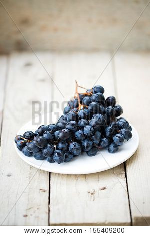 Bunch of ripe blue grapes on a light wooden background. Fresh autumn fruits. Light food photography.
