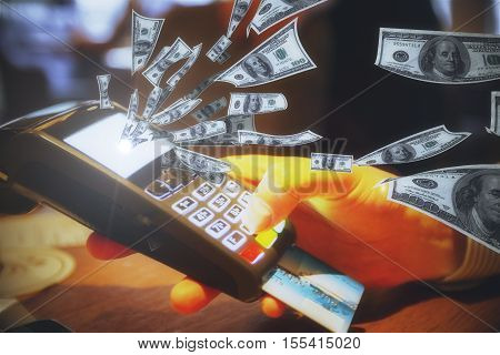 Hand holding POS terminal with credit card and abstract dollar bills flying out of screen. Money concept
