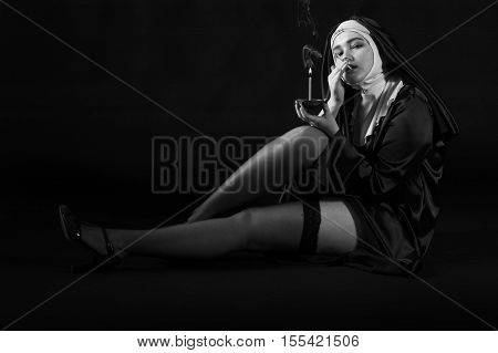 Sexy nun lights a cigarette from church candle.