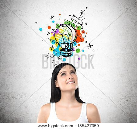 Smiling woman in white tank top standing under colorful light bulb sketch drawn on concrete wall above her head. Concept of creative approach to problem solving
