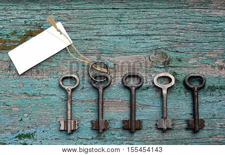 Door key with blank card for the text among other ones on old wooden background