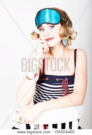 beautiful young woman in a striped dress and points for sleep, sitting on a chair and posing. sleeping eye covering mask.