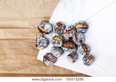 Roasted chestnuts served on white and brown craft paper with copy space. Delicious grilled chestnuts on old wooden table close up