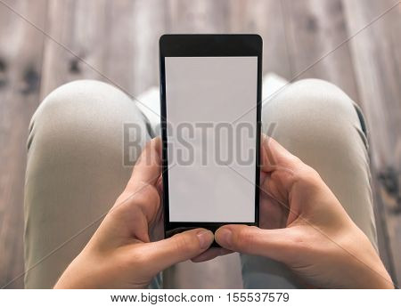 Young girl sitting with a phone in hands, uses the touchscreen, blue jeans, wooden background