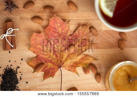 autumn and ethnoscience concept - cup of lemon tea and honey on wooden board with maple leaf and almond