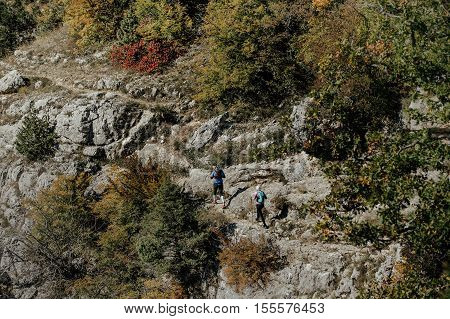 man and woman runner with walking poles and a backpack runs along cliff steep