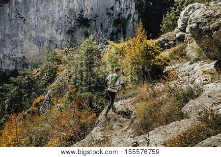 male runner with walking poles and a backpack runs along cliff steep
