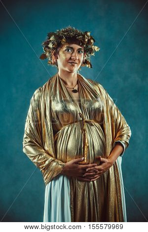 Pregnant Woman In Golden Toga And Wreath Posing Like A Greece Fertility Goddess