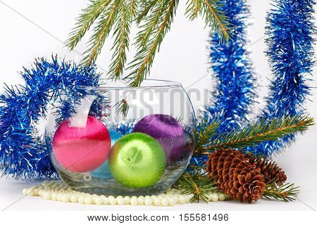 Colored christmas balls in a glass vase among fluffy blue tinsel and fir-tree brunches on white background
