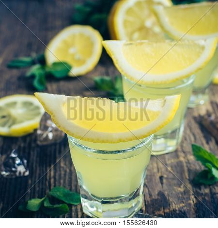 Traditional homemade lemon liqueur limoncello and fresh citrus on the old wooden background. Italian traditional liqueur limoncello with lemon. Italian alcoholic beverage. Selective focus. Square.