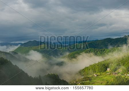 Mountain Forest With Fog Against Dramatic Sky On The Background