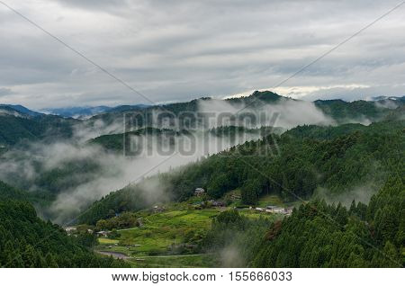 Aerial landscape of Japanese village and farms in goffy morning with clouds on mountain slopes. Yotsuya no Semmaida Shinshiro Japan
