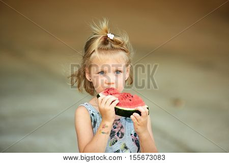 Adorable blonde girl eats a slice of watermelon outdoors