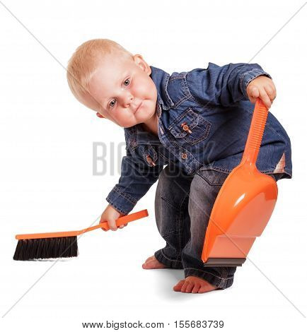 Cute little boy in a blue shirt and jeans, holding a dustpan having bent and sweeping brush isolated on white background.