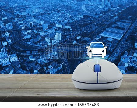 Wireless computer mouse with car front view flat icon on wooden table over aerial of city tower street and expressway Internet service car concept
