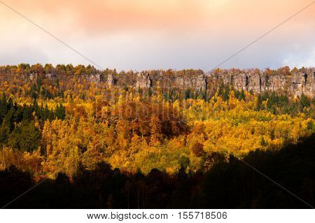Panoramic view of sandstone rock formation in the middle of colorful autumn forest. Dramatic evening view. Tisa Rocks, aka Tiske Walls, Czech-Saxon Switzerland, Czech Republic