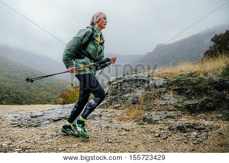 Yalta Russia - October 8 2016: runner middle-aged woman running in rain on a mountain trail with walking poles during Crimea mountain marathon