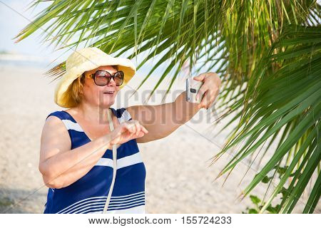 Adult woman photographing selfie by telephone in sunny beach day